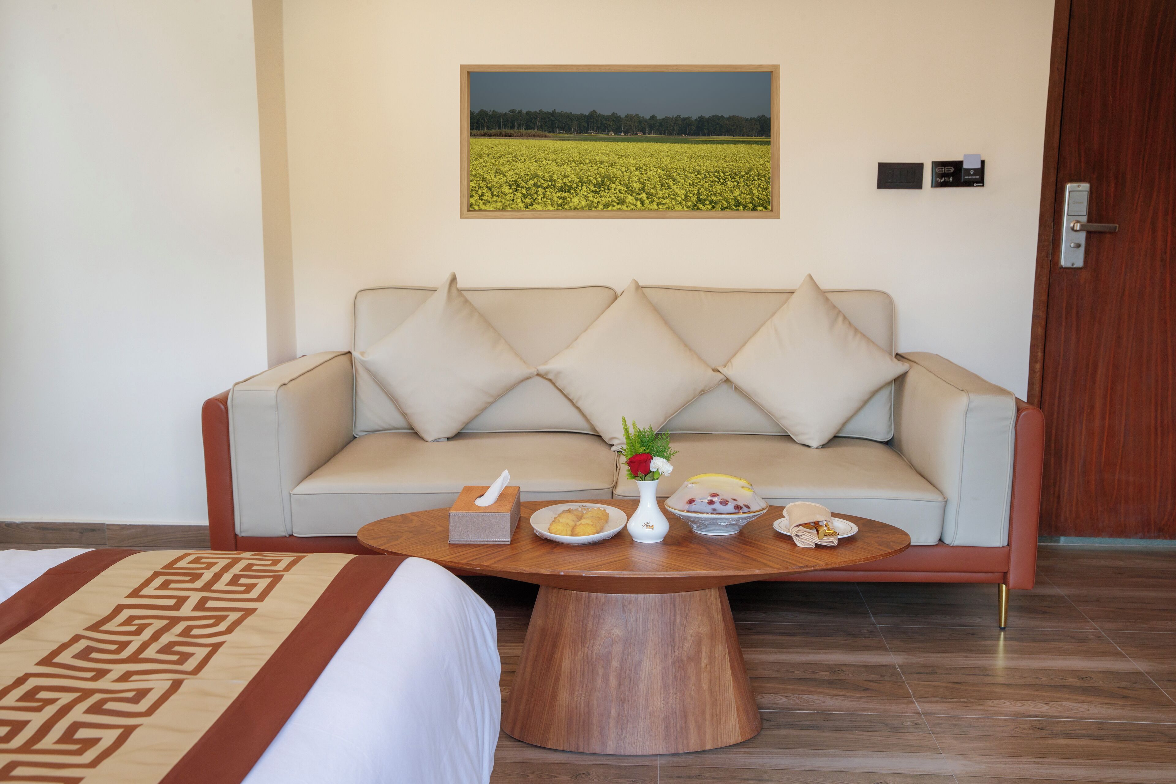A room with a sofa, a coffee table with food items, a painting of a field, and a door with a lock.