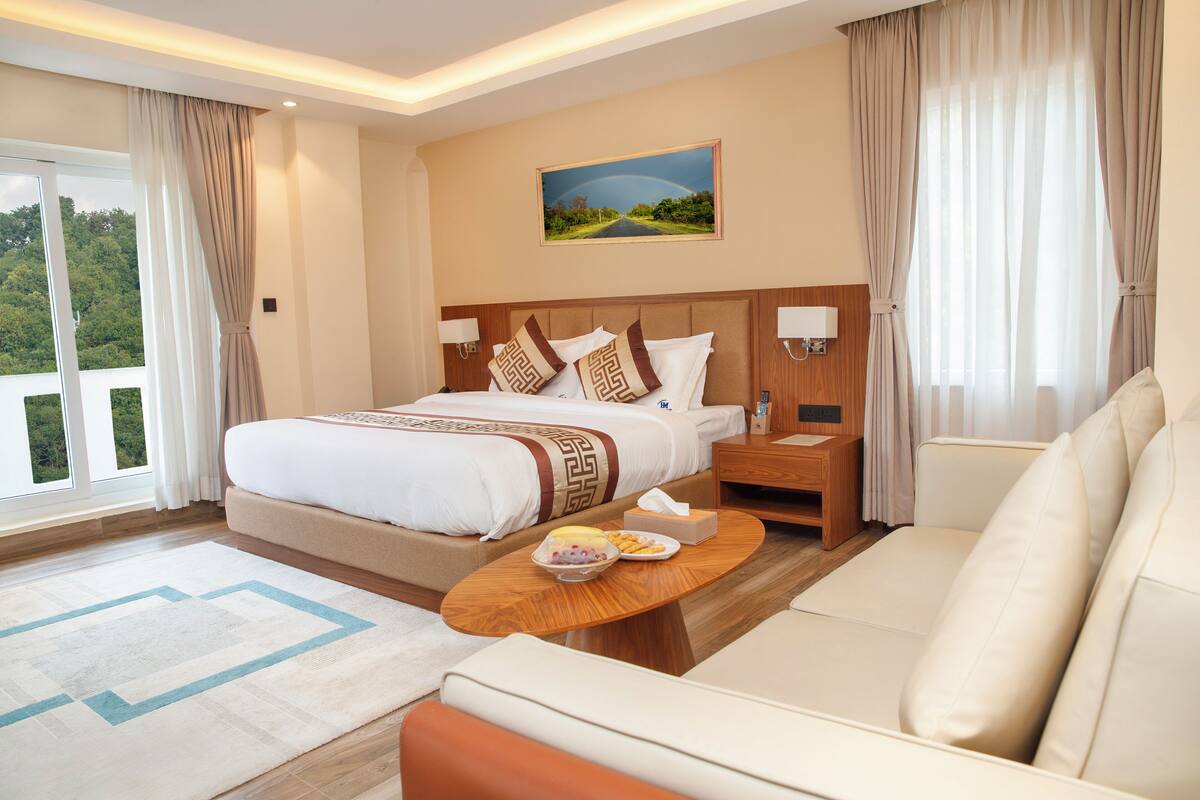 Habitación de hotel con una cama grande, un sofá, una mesita de madera y un cuadro en la pared.