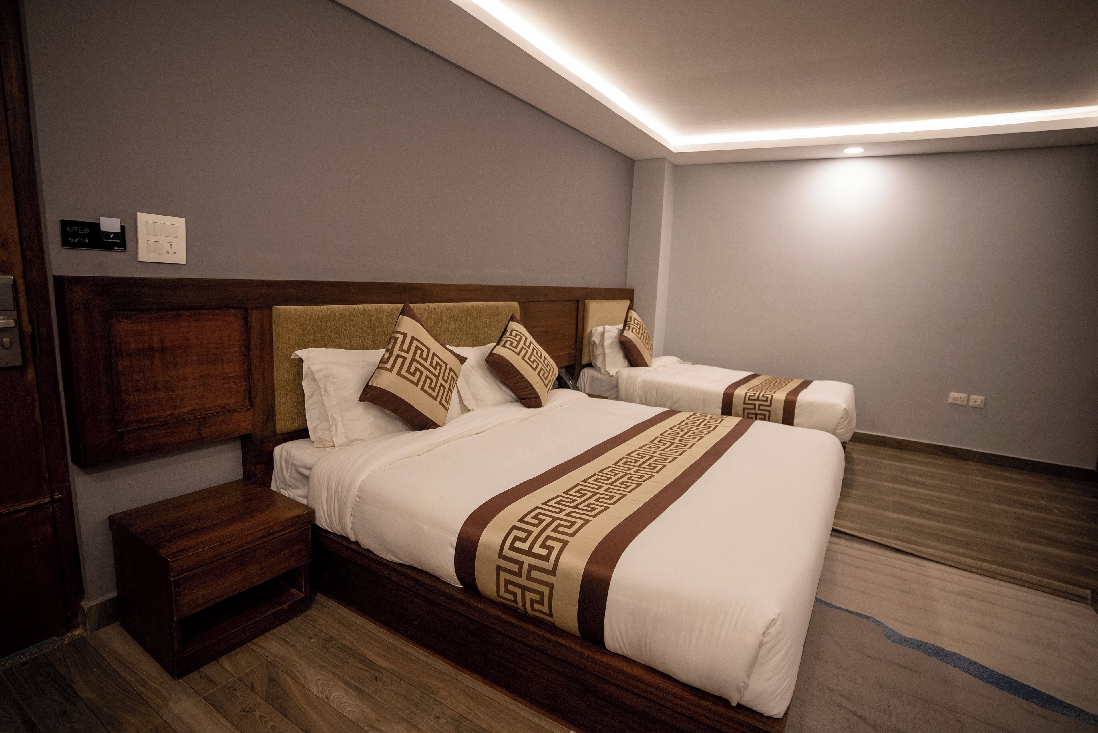 A hotel room with two beds, wooden headboards, and a modern ceiling light fixture.