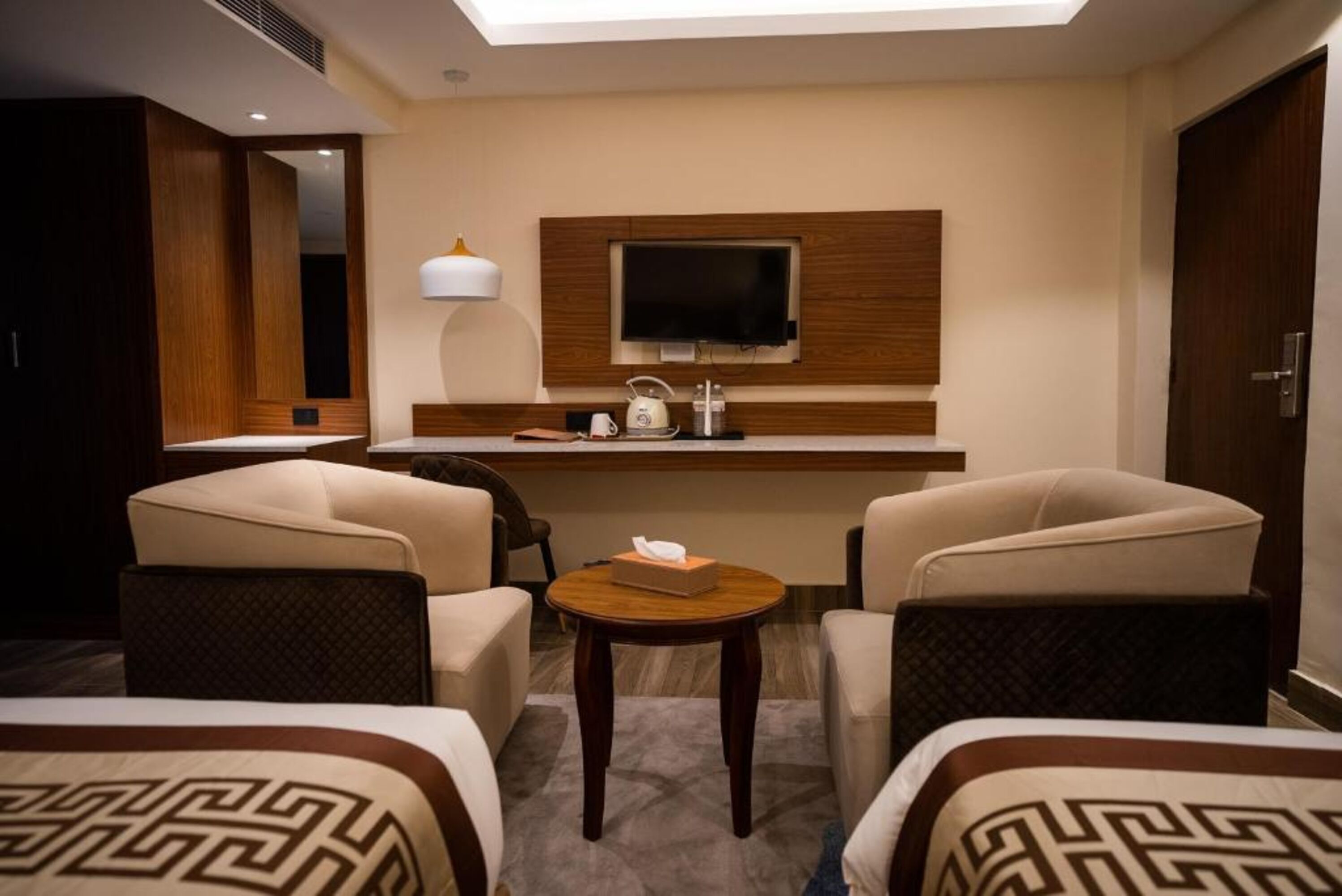 A hotel room with two beds, a small desk with a TV, a lamp, and a coffee machine.