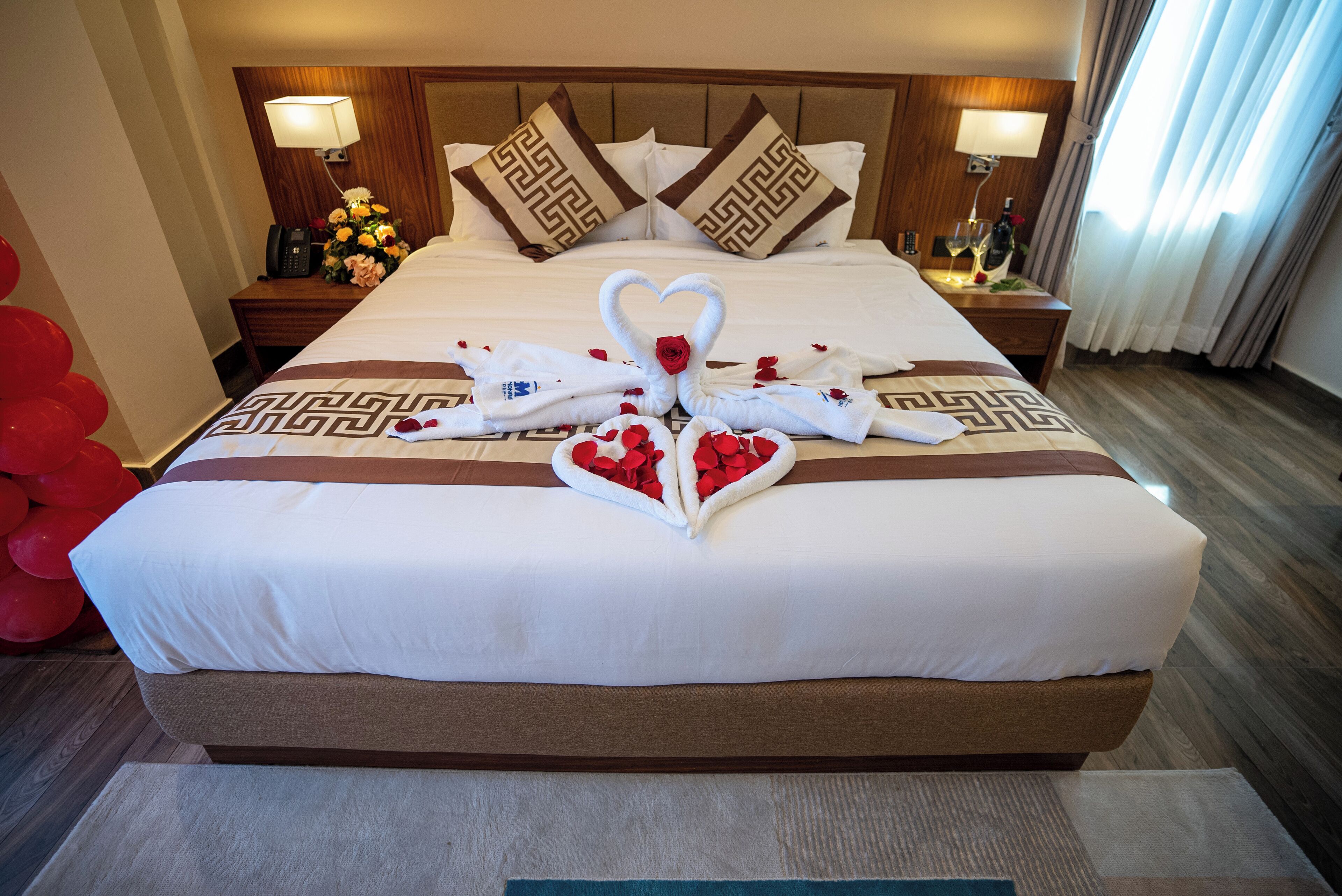 A hotel room with a large bed, a wooden headboard, two bedside tables with lamps, and a floral arrangement on one table.
