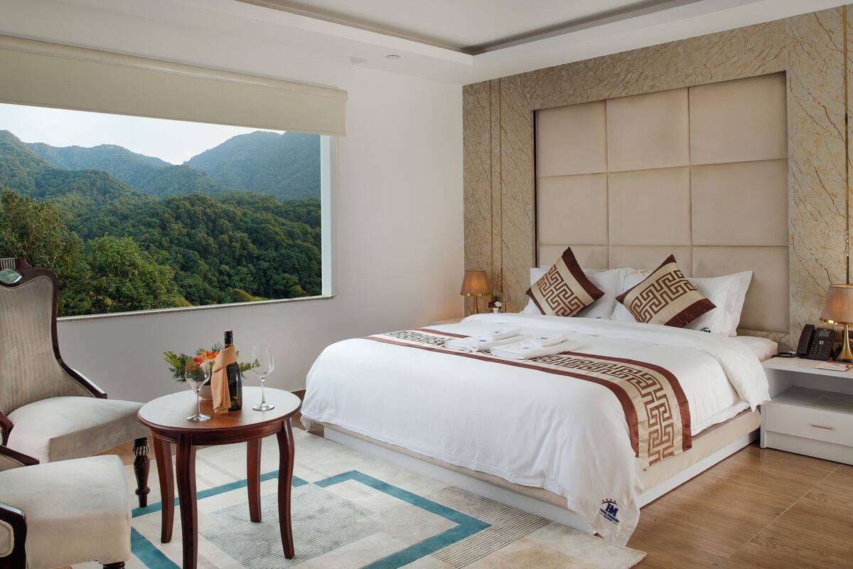 Habitación de hotel con una cama grande, zona de estar con una mesa, vista a las montañas y pared con diseño de mármol.
