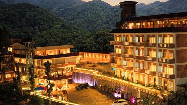 A hotel with multiple floors, a swimming pool, and a mountainous backdrop. - Nagarjun Resort (Tarakeshwar)
