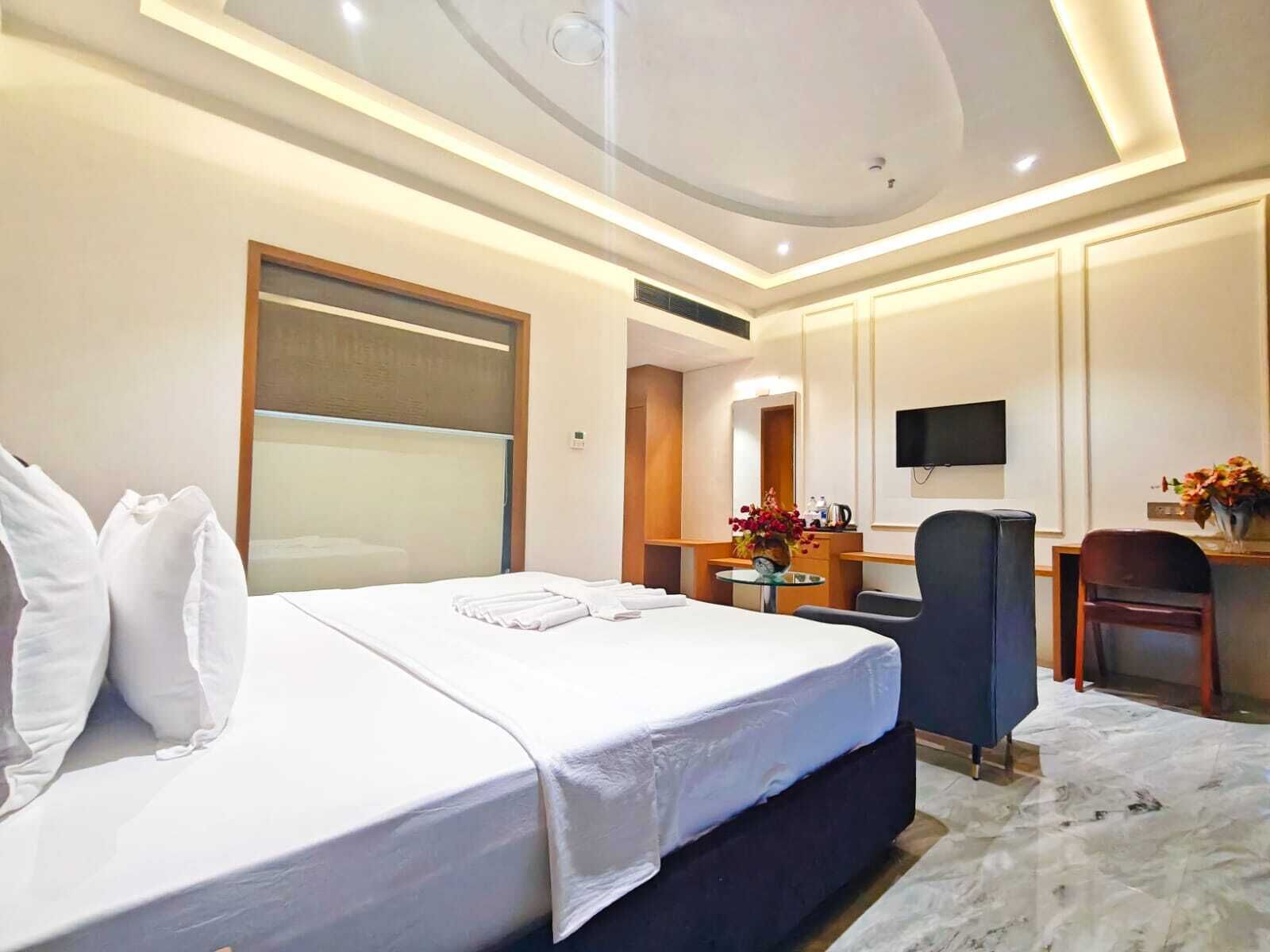 Een hotelkamer met een groot bed, een bureau, een stoel, een televisie en een bijzettafeltje met bloemen.