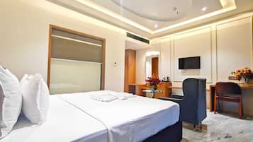 A hotel room with a large bed, a desk, a chair, a TV, and a small table with flowers.