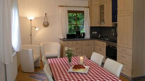 Una cocina acogedora con una mesa de comedor para cuatro personas, armarios de madera y una ventana con vistas a la vegetación.