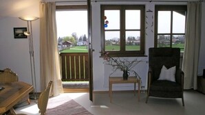 Una habitación con una mesa de comedor, sillas, un sofá, una mesita con un jarrón y vistas a un paisaje verde a través de una ventana.