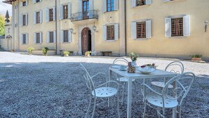 A building with a balcony, a table with chairs, and a gravel courtyard.