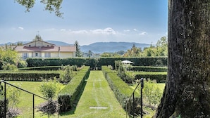 A well-maintained garden with a central pathway leading to a building with a red roof.