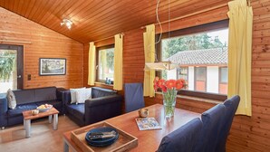 L’intérieur chaleureux d’un chalet avec des murs en bois, un coin repas comprenant une table et des chaises, un canapé et une fenêtre avec des rideaux.