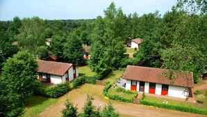 Un ensemble de petits bâtiments blancs, rehaussés d’éléments rouges, entourés d’une végétation luxuriante et d’arbres.