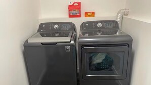 Two front-loading washing machines in a corner with a red and an orange box on the wall above them.