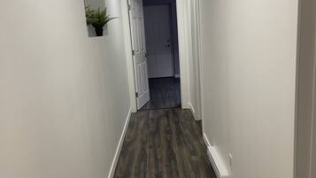 Un couloir avec un plancher en bois foncé, des murs blancs et une porte au fond.