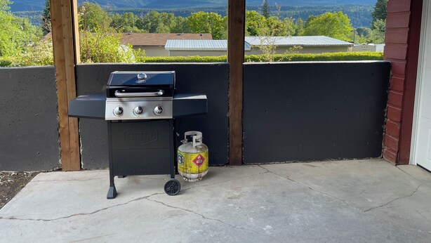 A barbecue grill with a propane tank, set against a backdrop of mountains and a clear sky.