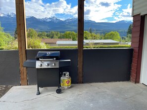 A barbecue grill with a propane tank, set against a backdrop of mountains and a clear sky.