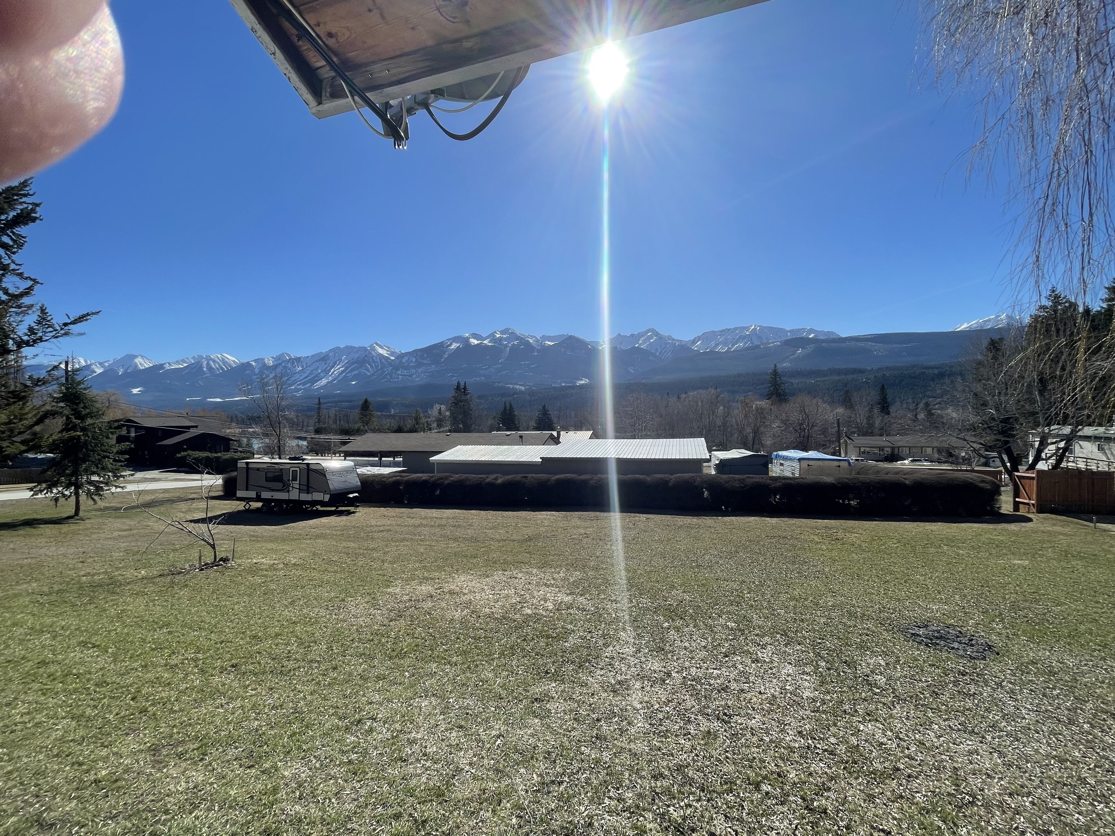 On peut clairement distinguer une chaîne de montagnes dont les sommets sont enneigés, un espace herbeux où est garé un camping-car, et un bâtiment doté d’un toit plat.