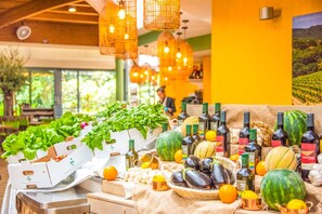 A table with fresh produce, including leafy greens, tomatoes, and citrus fruits, in a brightly lit indoor setting with hanging lights.