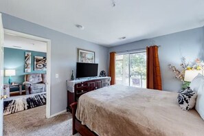 Un dormitorio con una cama grande, un televisor en una cómoda, una silla y vistas al exterior.