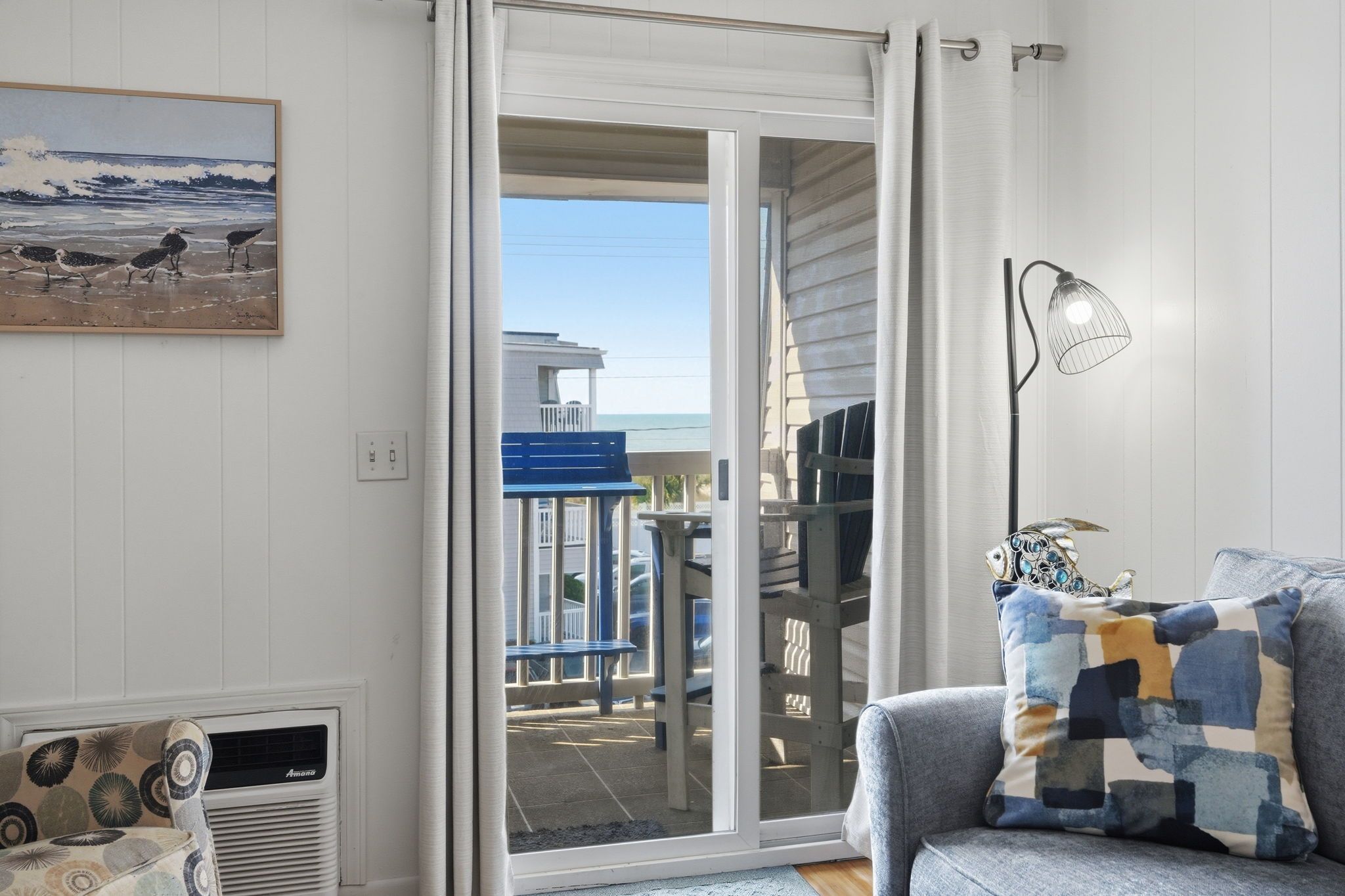 Une pièce avec vue sur la plage, un banc bleu, un coussin à motifs et une lampe.