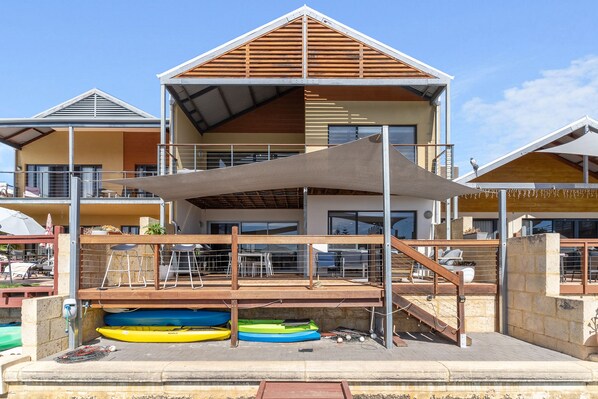 A multi-story building with a covered outdoor area, featuring a staircase, seating, and kayaks. - Piccolo Waters -  Two story coastal home , Located on the scenic Mandurah canals (Halls Head)