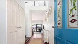 Un pasillo con puertas blancas, una puerta azul con detalles de vidrio decorativo, un tapete tejido y vistas a un espacio exterior.