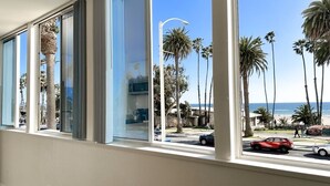 A hotel room with large windows overlooking a beach, palm trees, and a clear blue sky.
