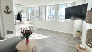 A modern living room with a large TV, a dining area, and a kitchen.