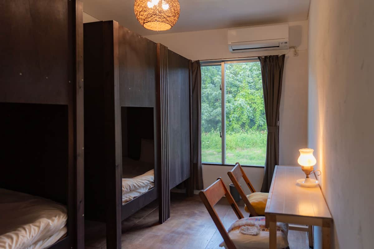 A room with bunk beds, a table with a lamp, and a window with curtains.