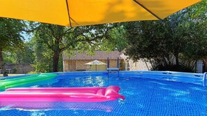 Piscina com chão em azulejo, rodeada por árvores e um edifício de pedra ao fundo.