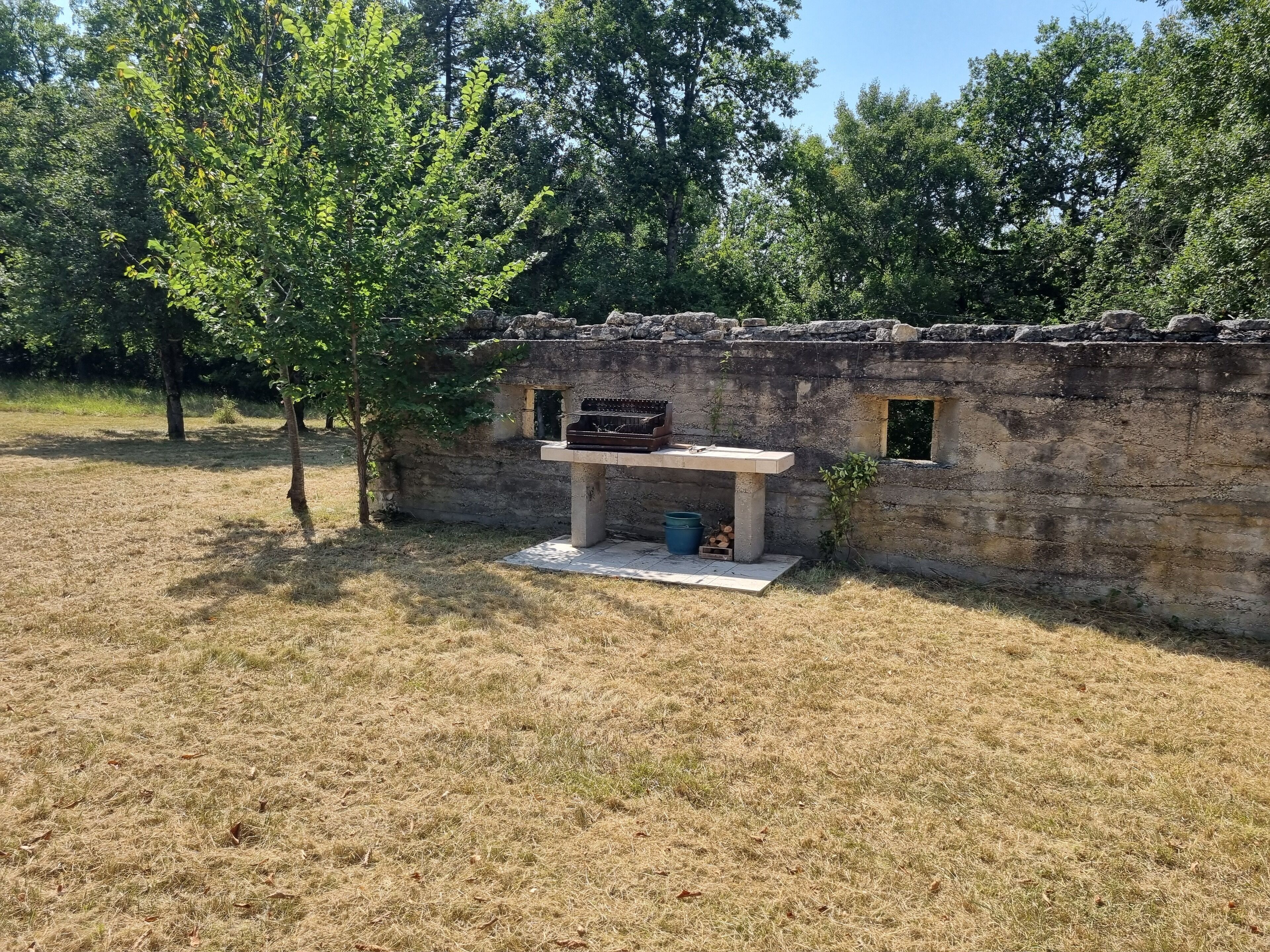 Un área de barbacoa rústica al aire libre con pared de piedra, una parrilla y un hogar.