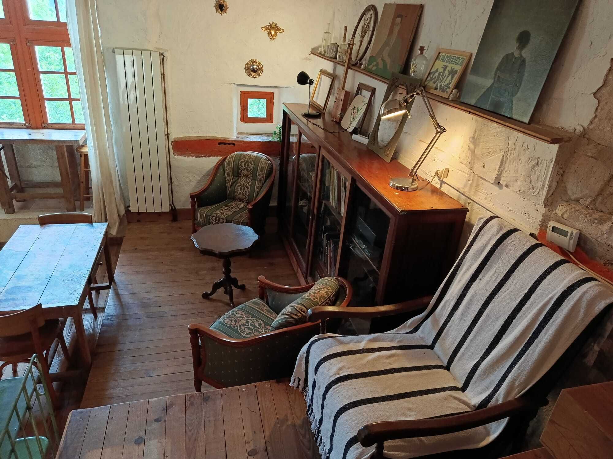 A cozy room with a wooden floor, a striped sofa, a wooden table, a chair, a bookshelf, and a fireplace.