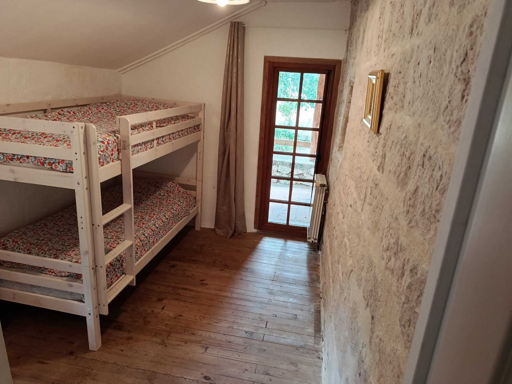 A room with bunk beds, a wooden floor, a door with a view, and a radiator.