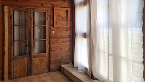 Um quarto de madeira com uma grande janela, uma porta com painéis de vidro e um candeeiro pendente amarelo.