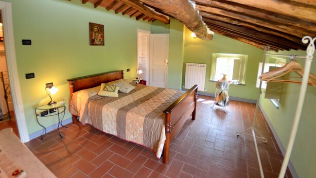 A bedroom with a wooden bed, a nightstand, a radiator, and a window with a view.