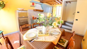 A dining area with a table set for four, chairs, a vase with flowers, and a kitchen in the background.