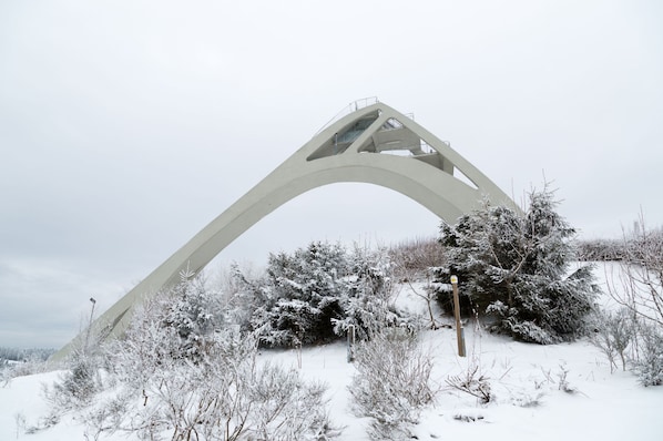 Uma grande estrutura de ponte branca e arqueada em meio a uma paisagem nevada com vegetação escassa.