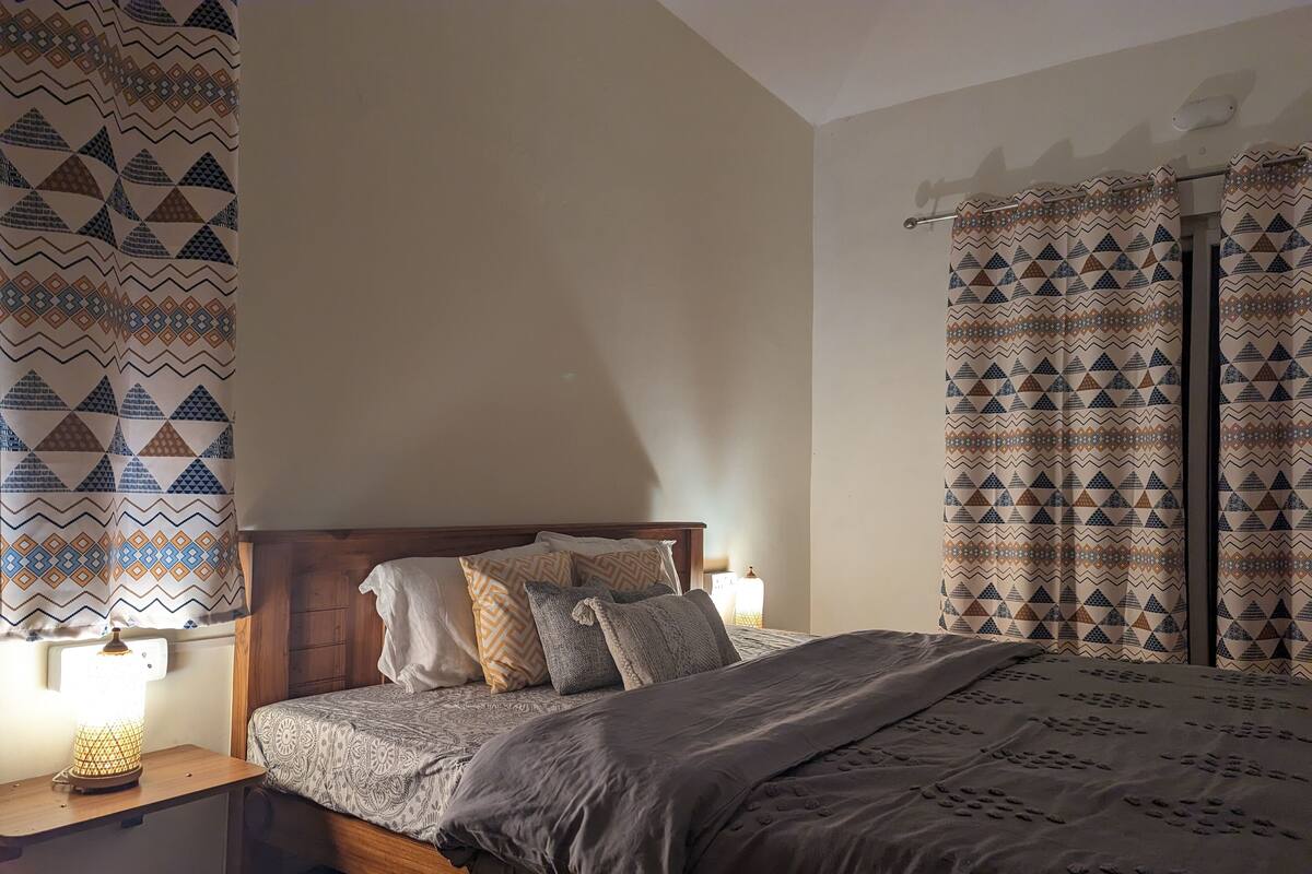 A bedroom with a wooden bed frame, patterned bedding, and curtains with a geometric design.