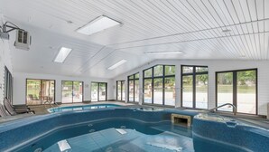 Een groot binnenzwembad met helder uitzicht op het buitenland, een overdekt dak en een zithoek met tafels en stoelen.