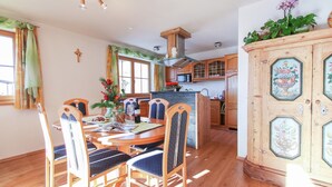 Un comedor con una mesa y sillas de madera, una cocina al fondo, y un mueble decorativo con diseños florales.