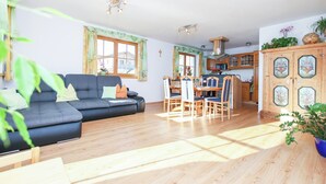 Sala de estar con sofá, mesa de comedor, sillas y una zona de cocina con armarios de madera y estufa.