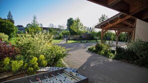 A foosball table in a covered outdoor area with a gravel path leading to a playground.