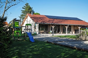 A building with a red-tiled roof, a covered patio area, and a playground with a blue slide.