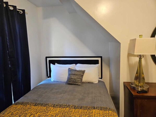 A bedroom with a bed, a bedside table with a lamp, and a curtain.