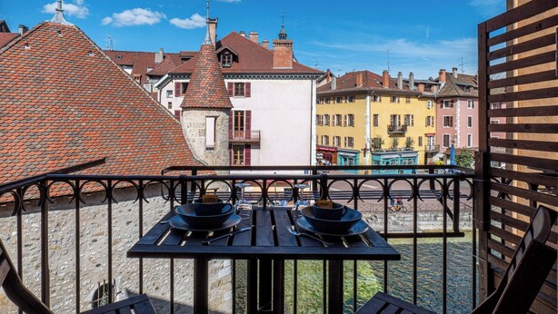 A balcony with a table set for two, overlooking a canal with buildings in the background.