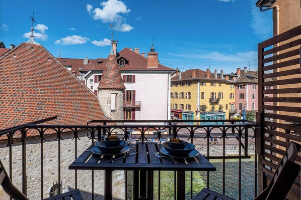 A balcony with a table set for two, overlooking a canal with buildings in the background.