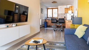 A modern living room with a flat-screen TV, a sofa, a coffee table, and a kitchen area in the background.