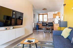 A modern living room with a flat-screen TV, a sofa, a coffee table, and a kitchen area in the background.