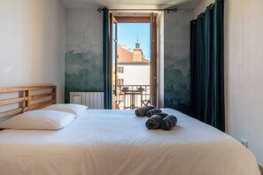 A hotel room with a bed, a wooden headboard, a view of a balcony with a table and chairs, and a window with curtains.