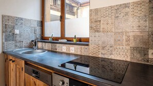 A kitchen with a double sink, wooden cabinets, a window with a view, and patterned tiles.