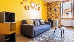 A living room with a sofa, a TV, a small table, and a patterned wall.